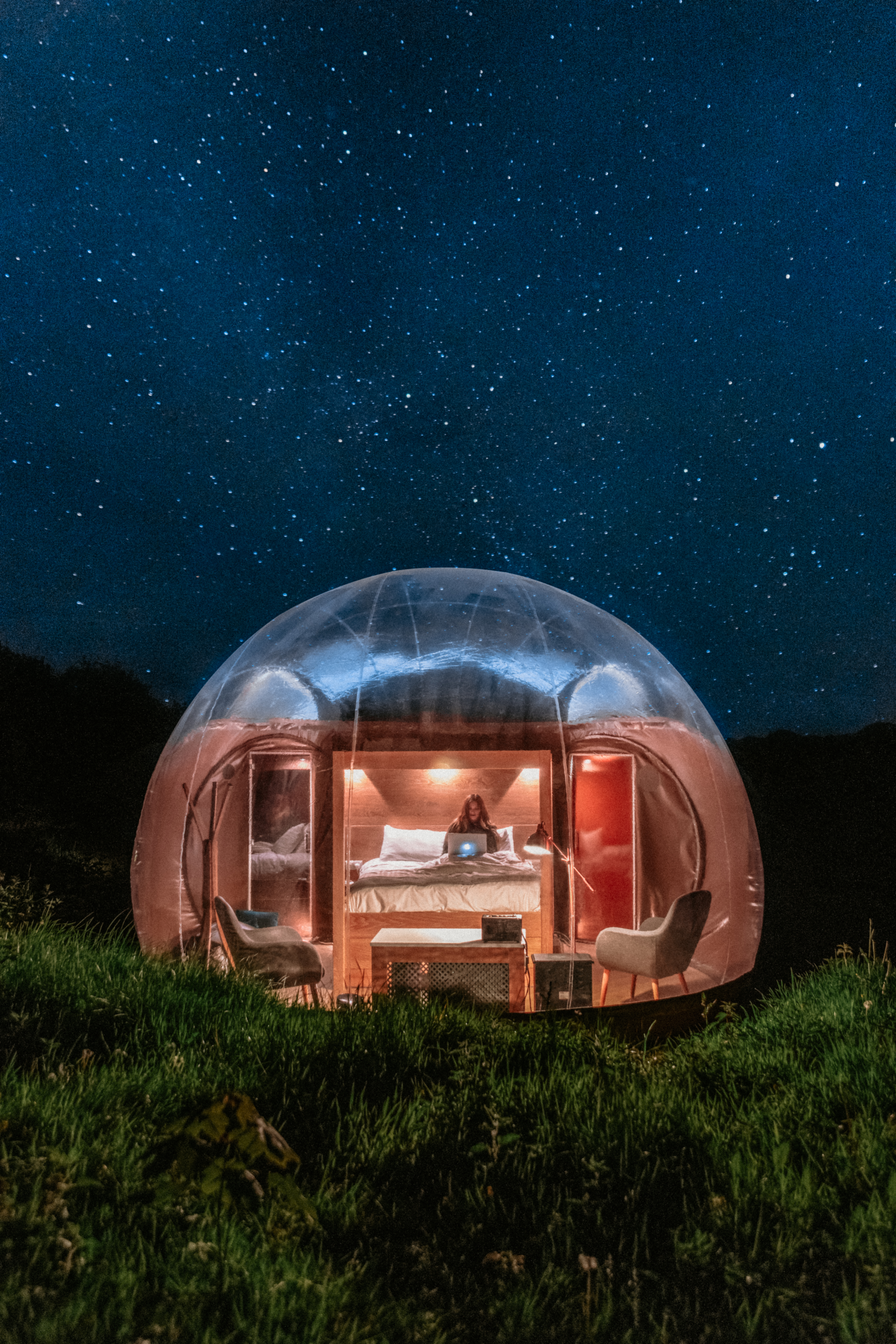 Woman in a bed in a glamping bubble pod at night