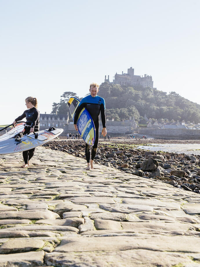 Windsurfers walking on a stone causeway that links an island to the mainland