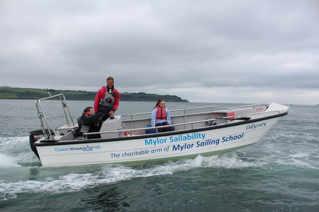 Man in a wheelchair steering a boat at sea accompanied by an instructor and woman