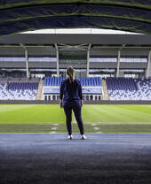 Mujer de pie frente al campo del estadio de la Academia del Manchester City.