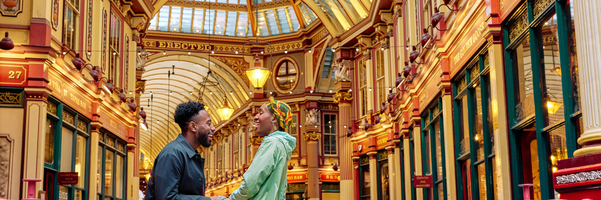 Smiling couple engaged in conversation outside a market hall with an ornate decorated gold ceiling.