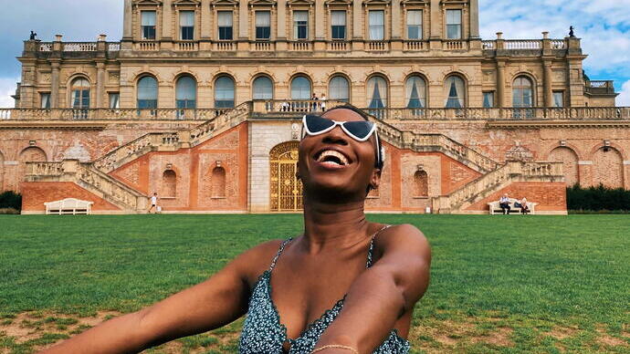 Woman laughing sitting on the grass in front of a stately home