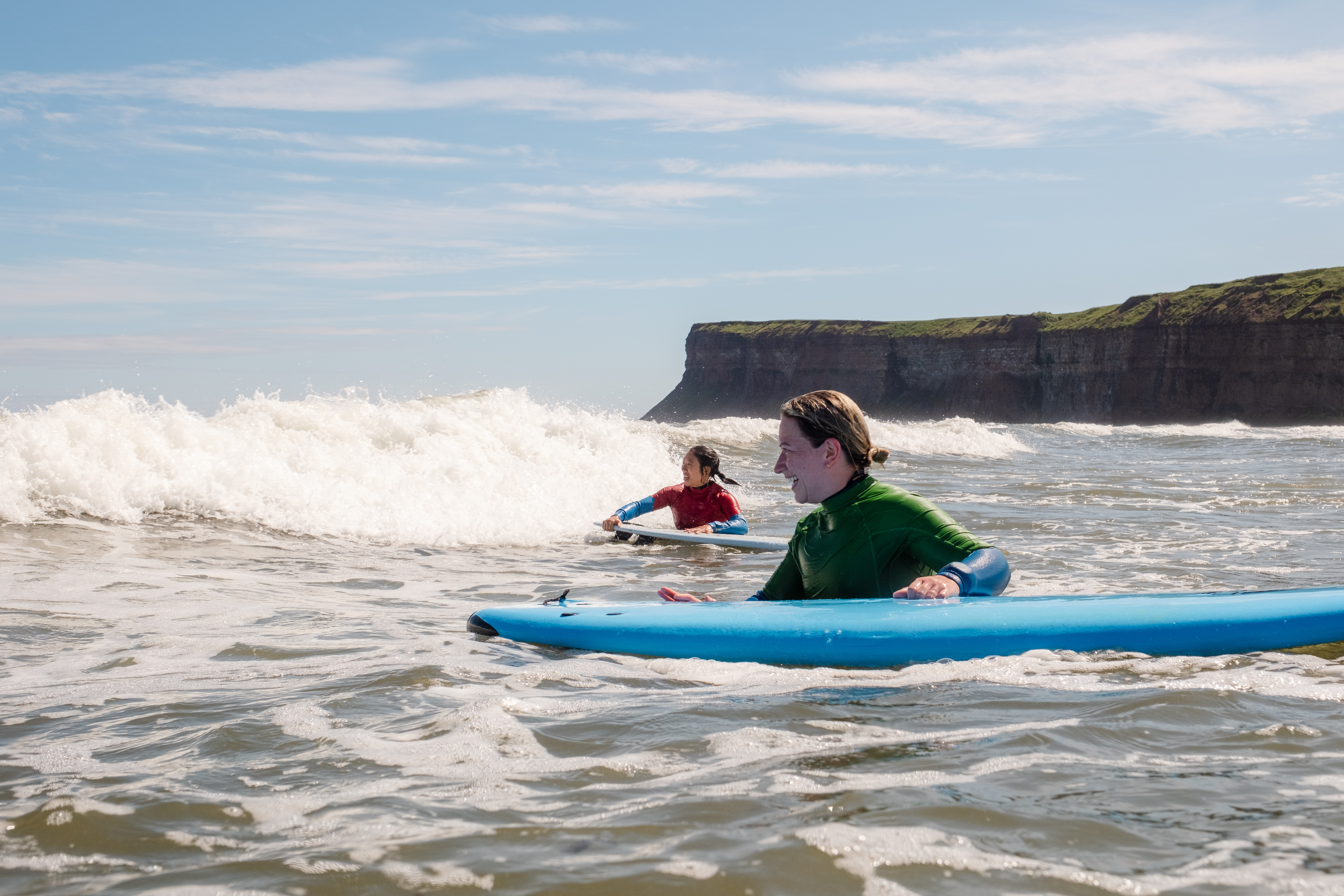 Dos mujeres sujetan tablas de surf mientras esperan las olas en el mar