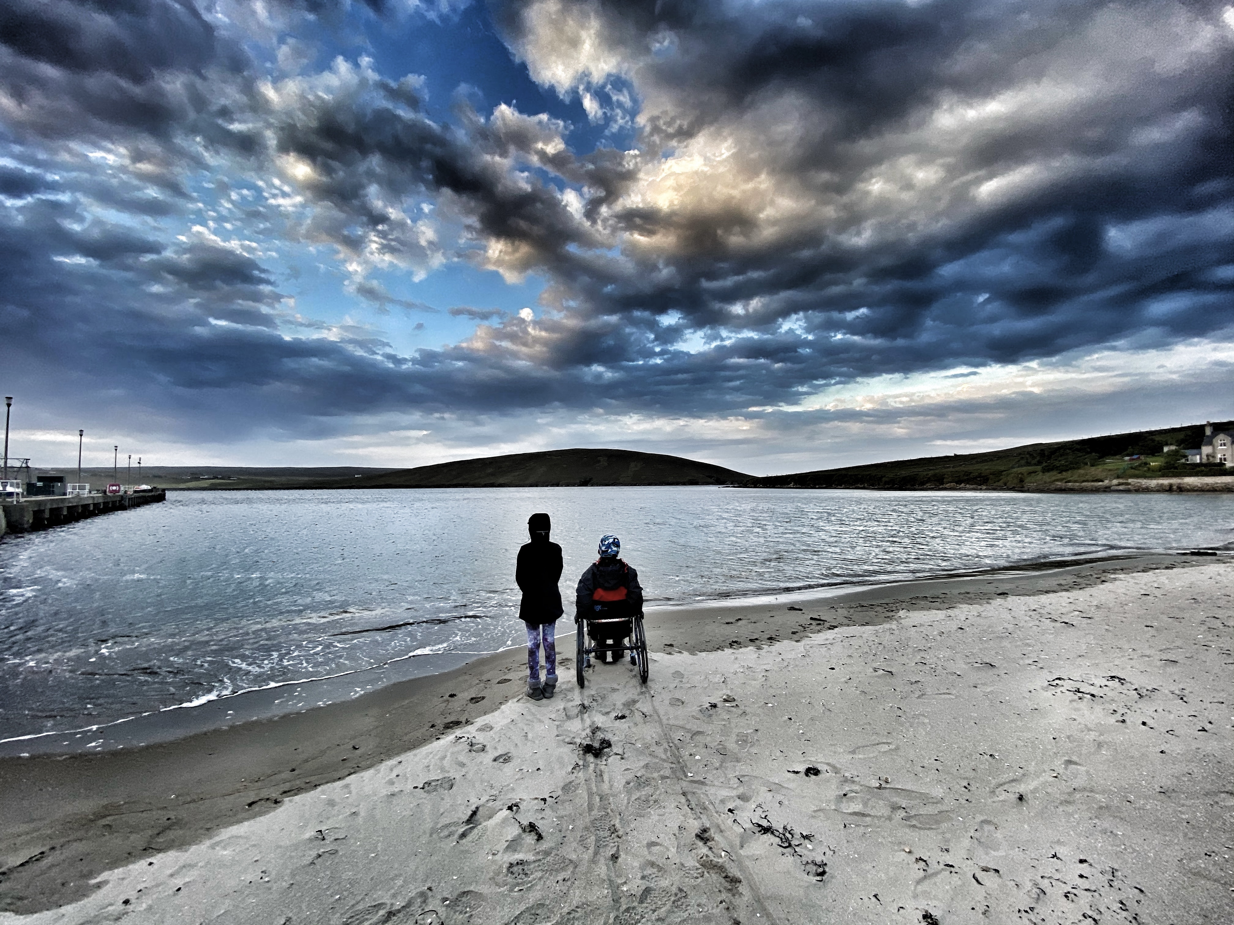 Wheelchair user and child on a beach looking out to sea