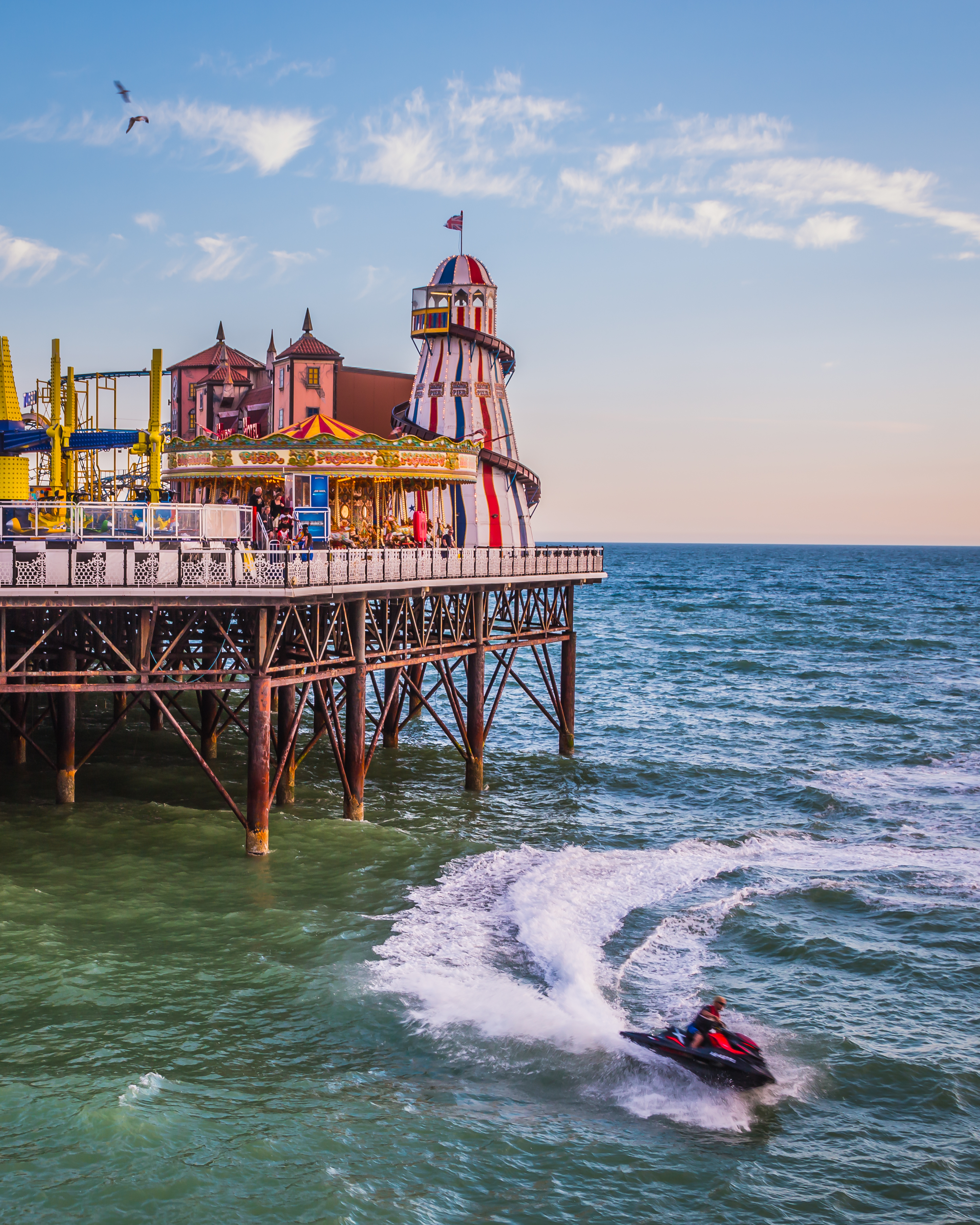 A fun fair on the end of a pier with a jet ski in the sea below