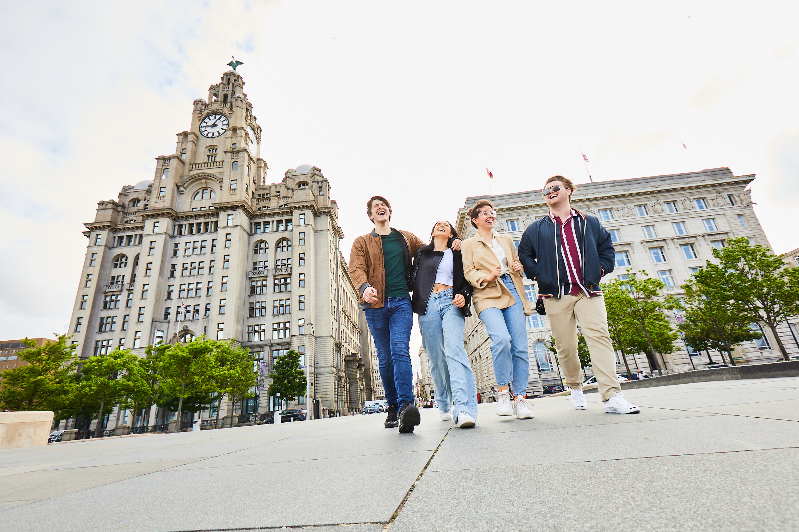 Four friends exploring a local city walking along waterfront promenade, with historic buildings in the background