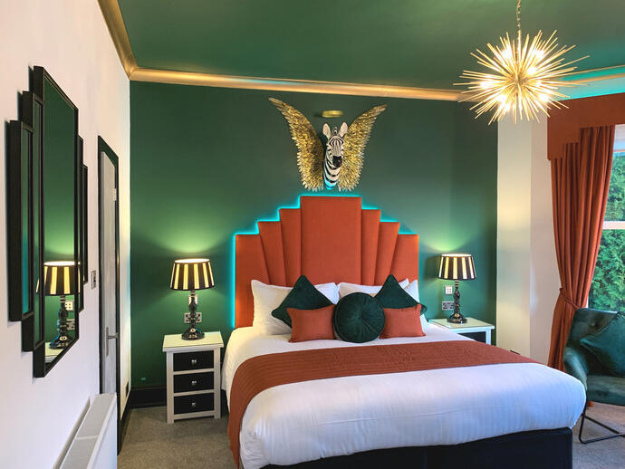View of a bedroom with a spiky light fitting and the head of a zebra in the centre of a pair of gold wings hung above the bed.