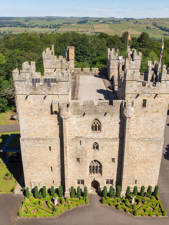 A shot of a fourteenth-century stone castle surrounded by trees and with fields in the distance. Langley Castle Hotel - Silver award winner for the Resilience and Innovation Award at the VisitEngland Awards for Excellence 2023.