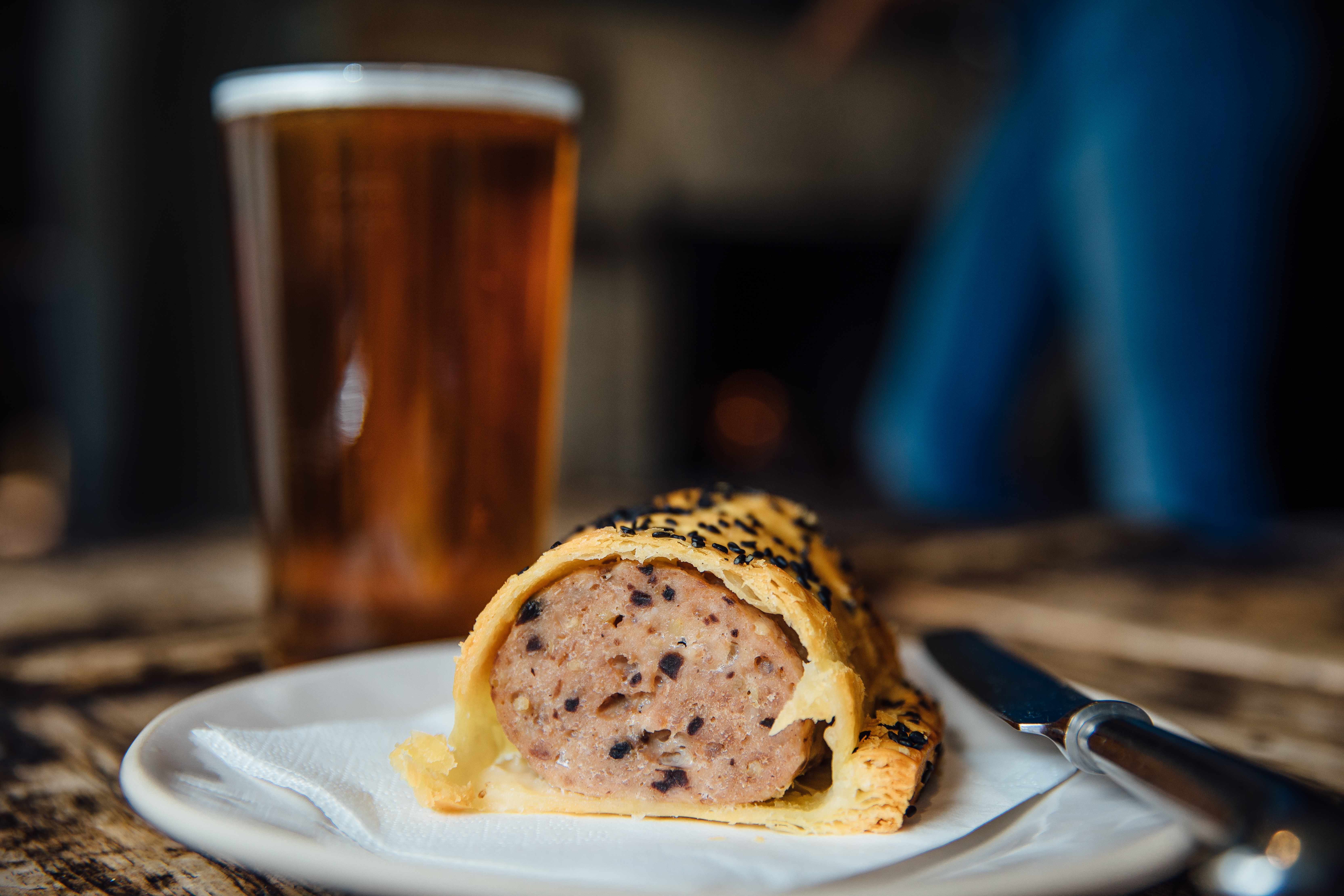 Pint of beer and a sausage roll on a plate on a table in a pub