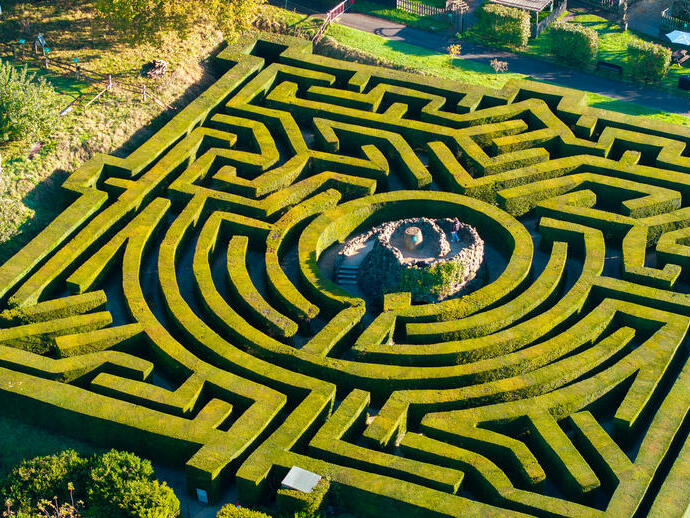 Luftaufnahme einer Frau, die den zentralen Turm eines Heckenlabyrinths hinaufsteigt