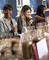 Three women participating in a whisky tasting session, seated at a table with several glasses of whisky in front of them.