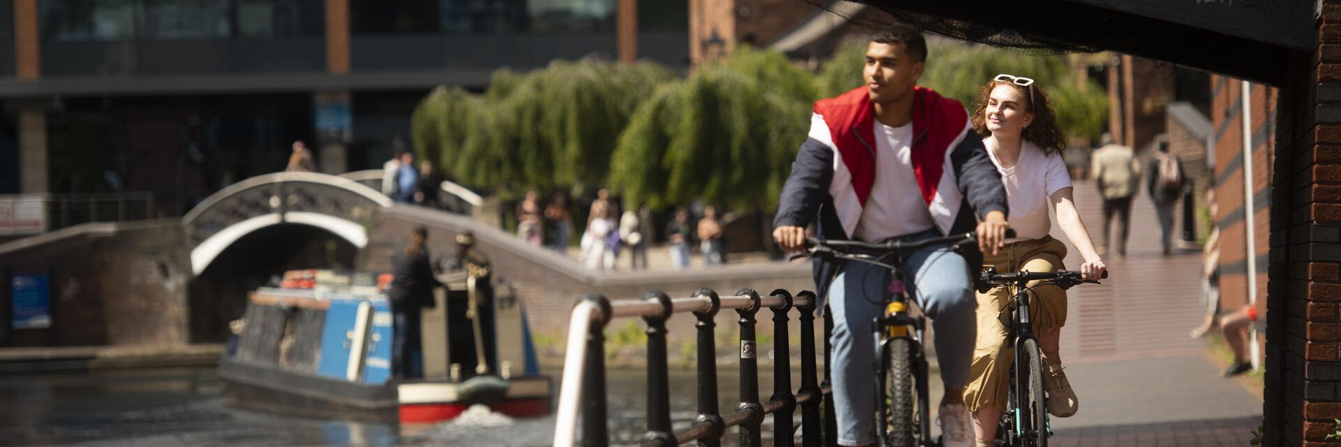 Ein Paar fährt mit dem Fahrrad eine Rampe parallel zu einem Kanal hinunter