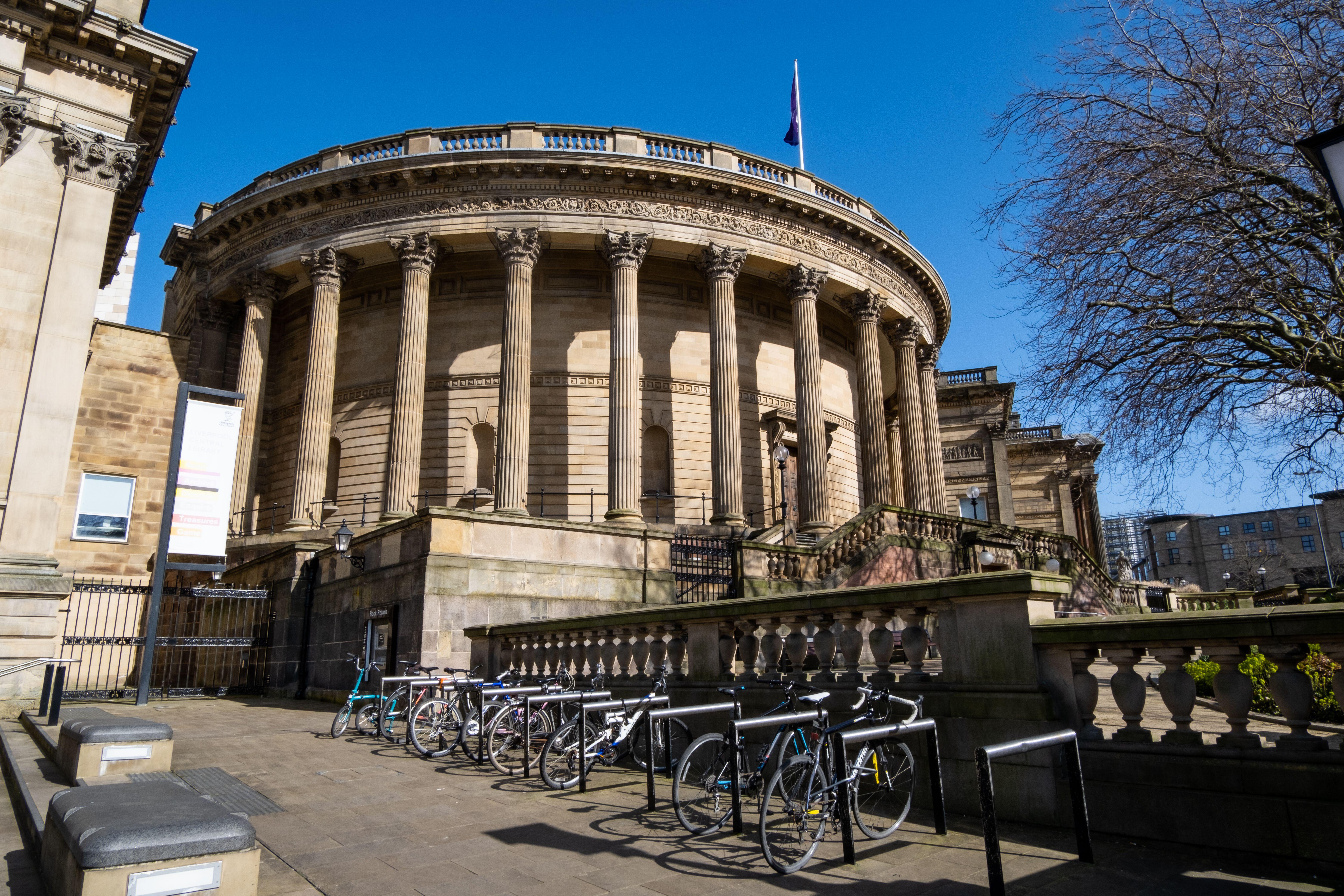 Historic circular building with columns, a flag on top, bicycles parked outside, and a tree visible to the right.