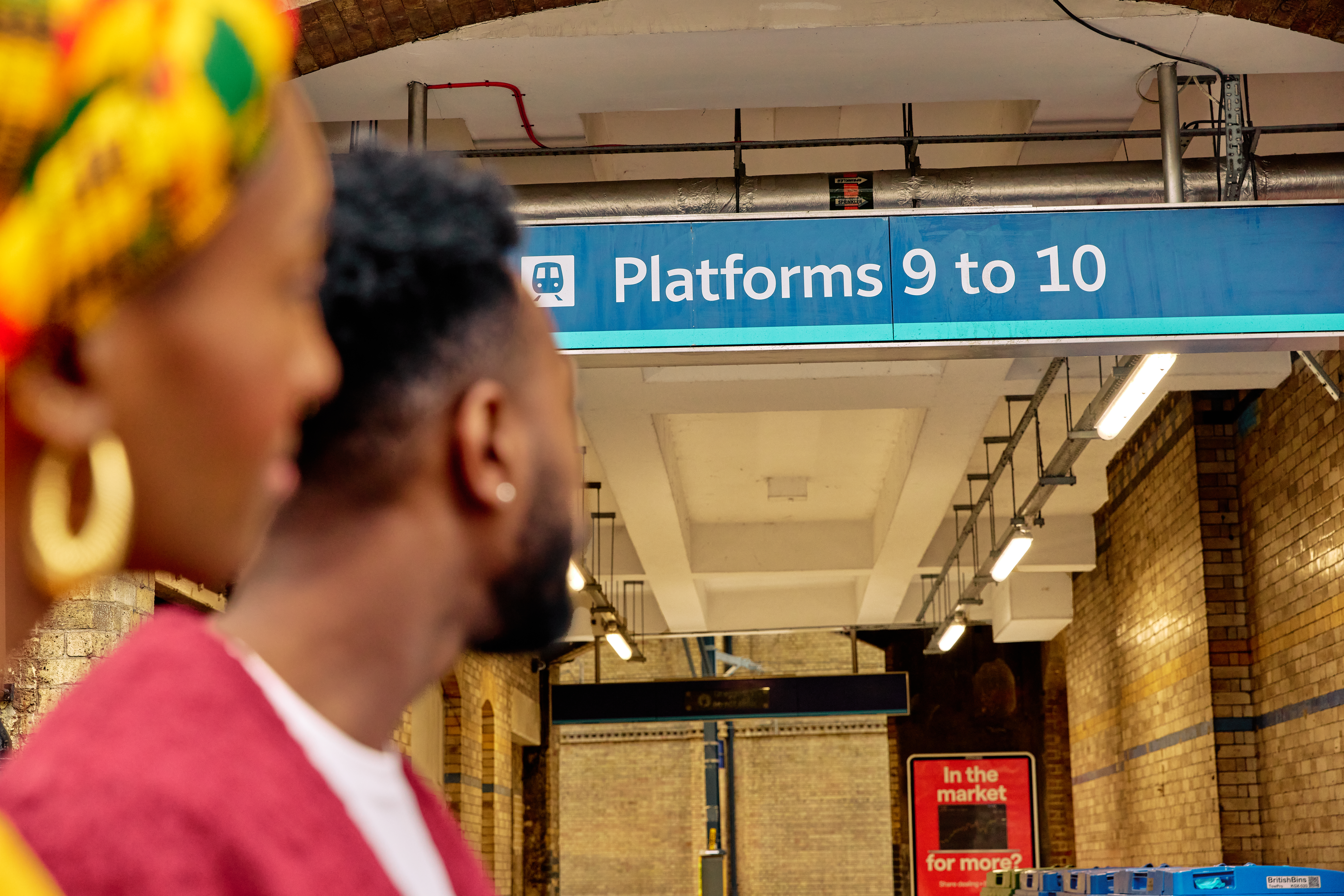 A couple look up at sign for Platforms 9 and 10 at a train station