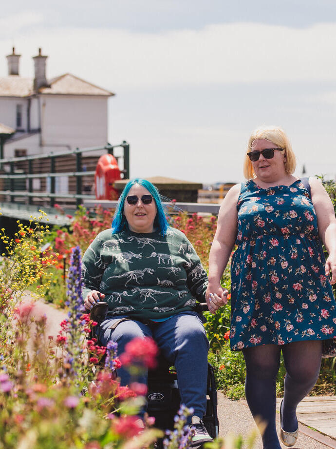 A woman walks with another women who sits in a wheelchair at an old railway station