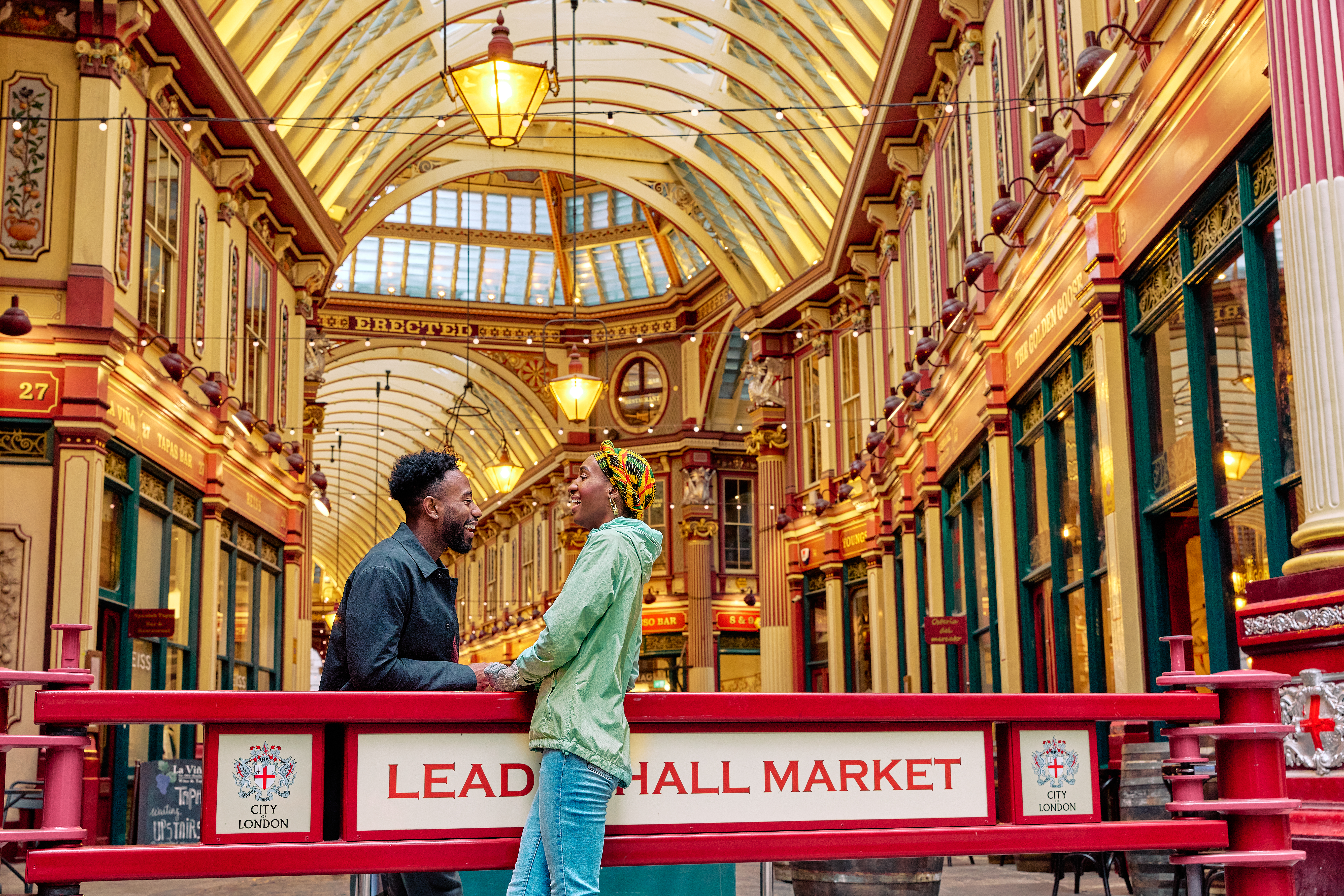 Smiling couple engaged in conversation outside a market hall with an ornate decorated gold ceiling.