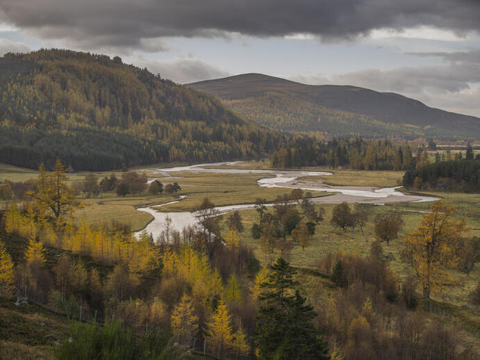 Landscape shot of a countryside view with a mountain backdrop and a stream running through the centre.
