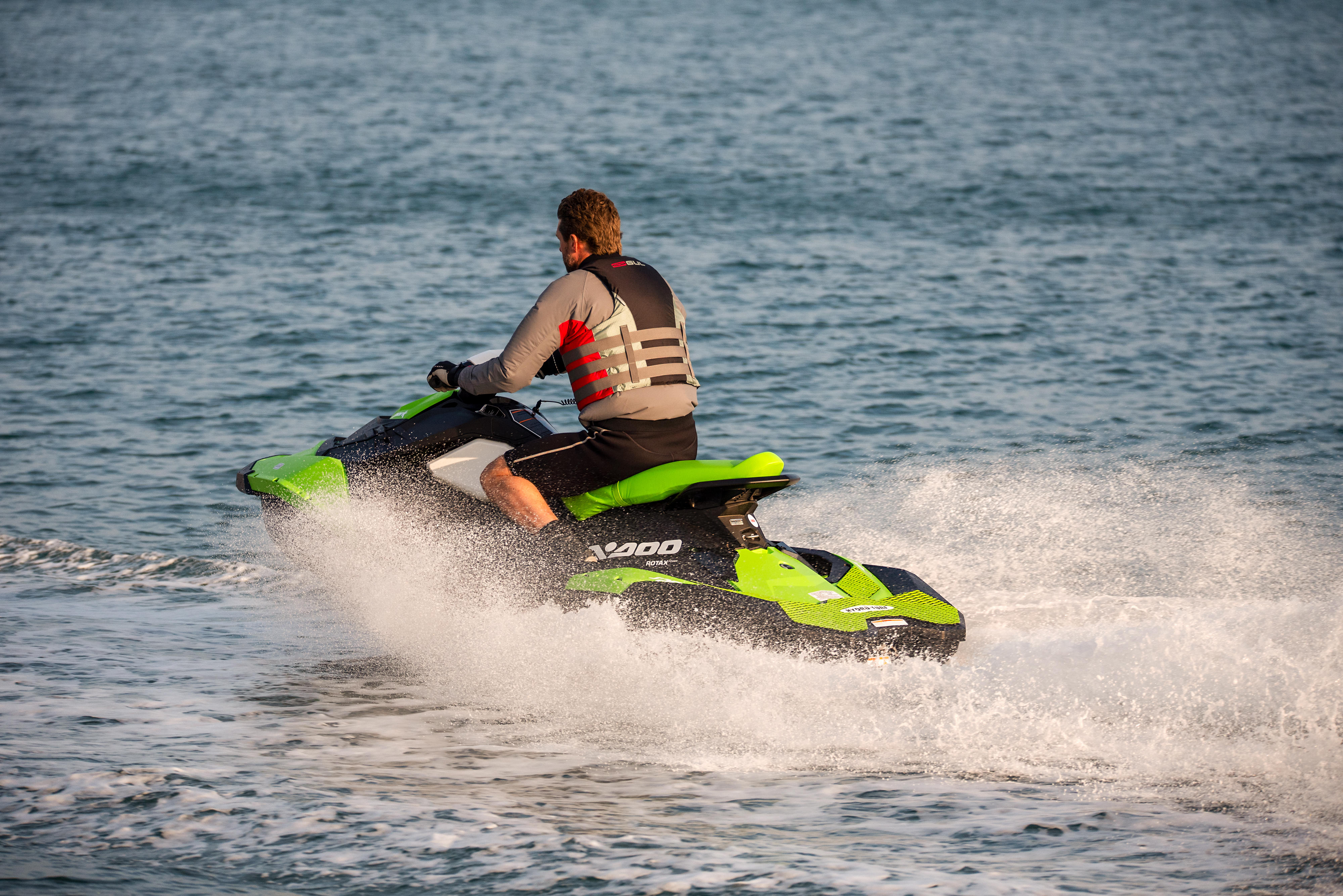 Middle aged man wearing a life vest rides a personal water craft Jet Ski along a calm sea.