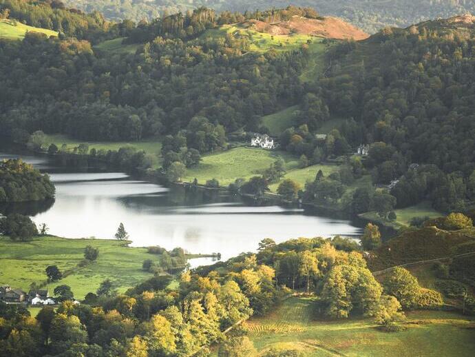 Two people sat on the edge of a fell looking over a green valley with a lake at the bottom
