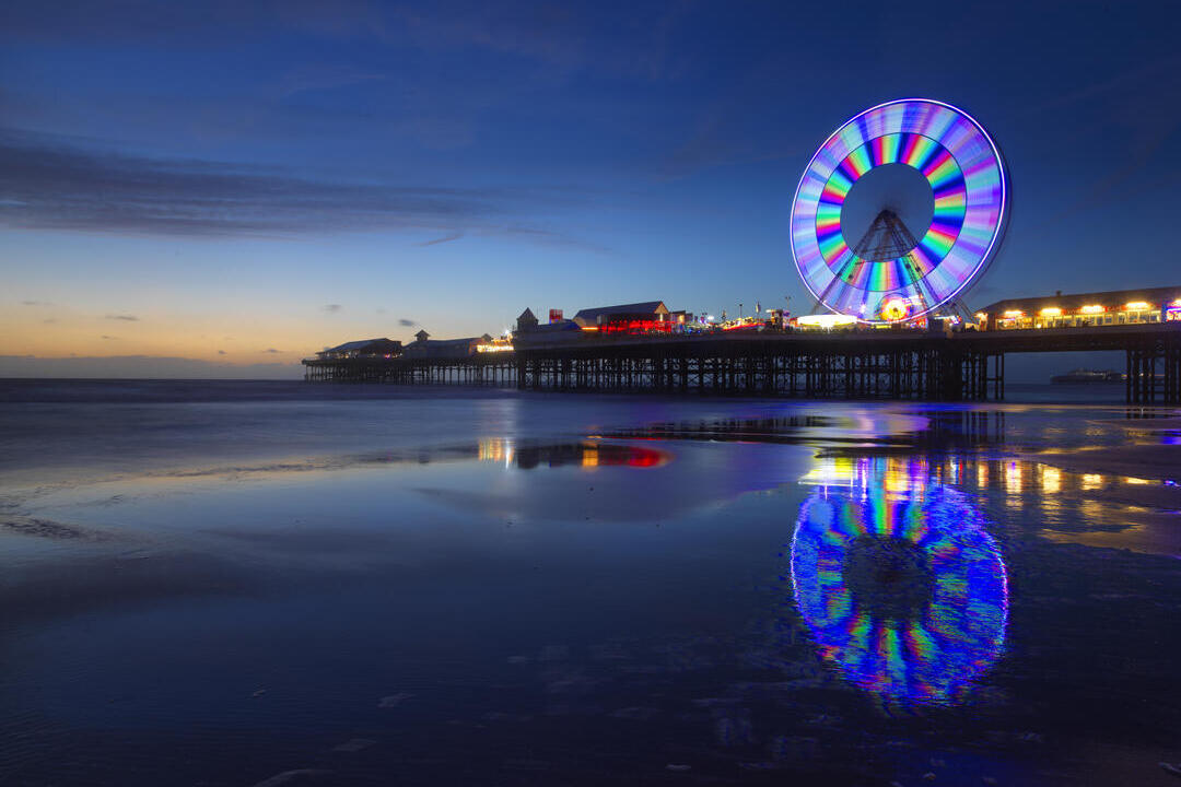 Colourful big wheel lit up on a pier at night.