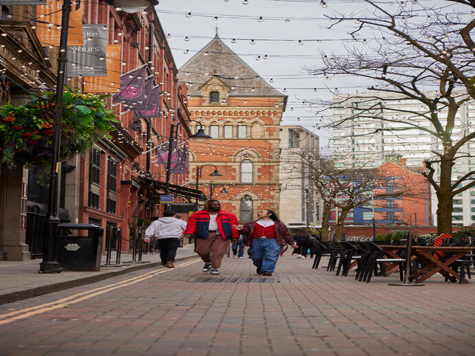 Two men chatting and walking down a street with cafes and a canal.
