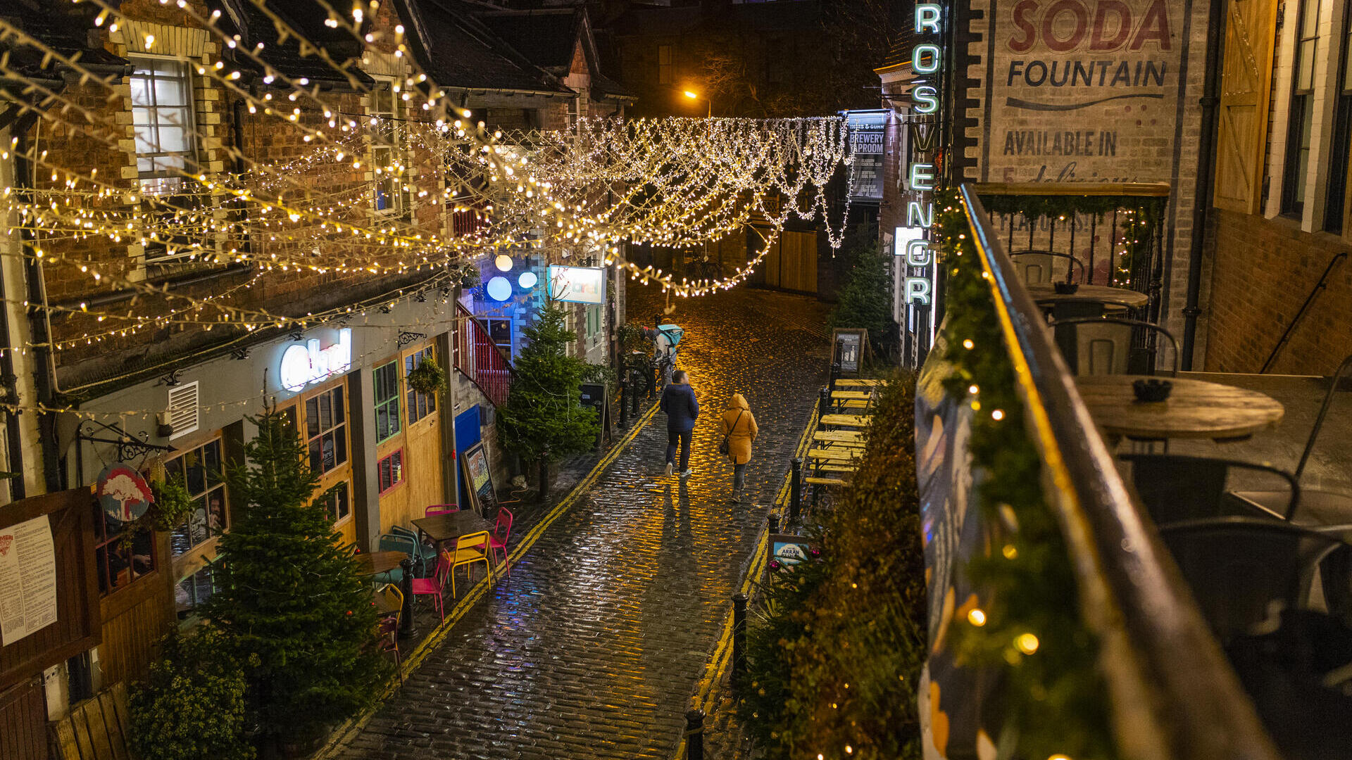 Couple walking along a cobbled street at night hung with fairy lights