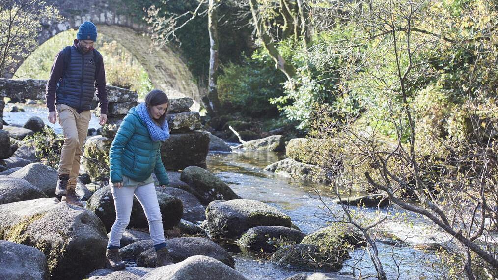 Pareja haciendo equilibrio sobre rocas junto a un arroyo cerca de unos árboles