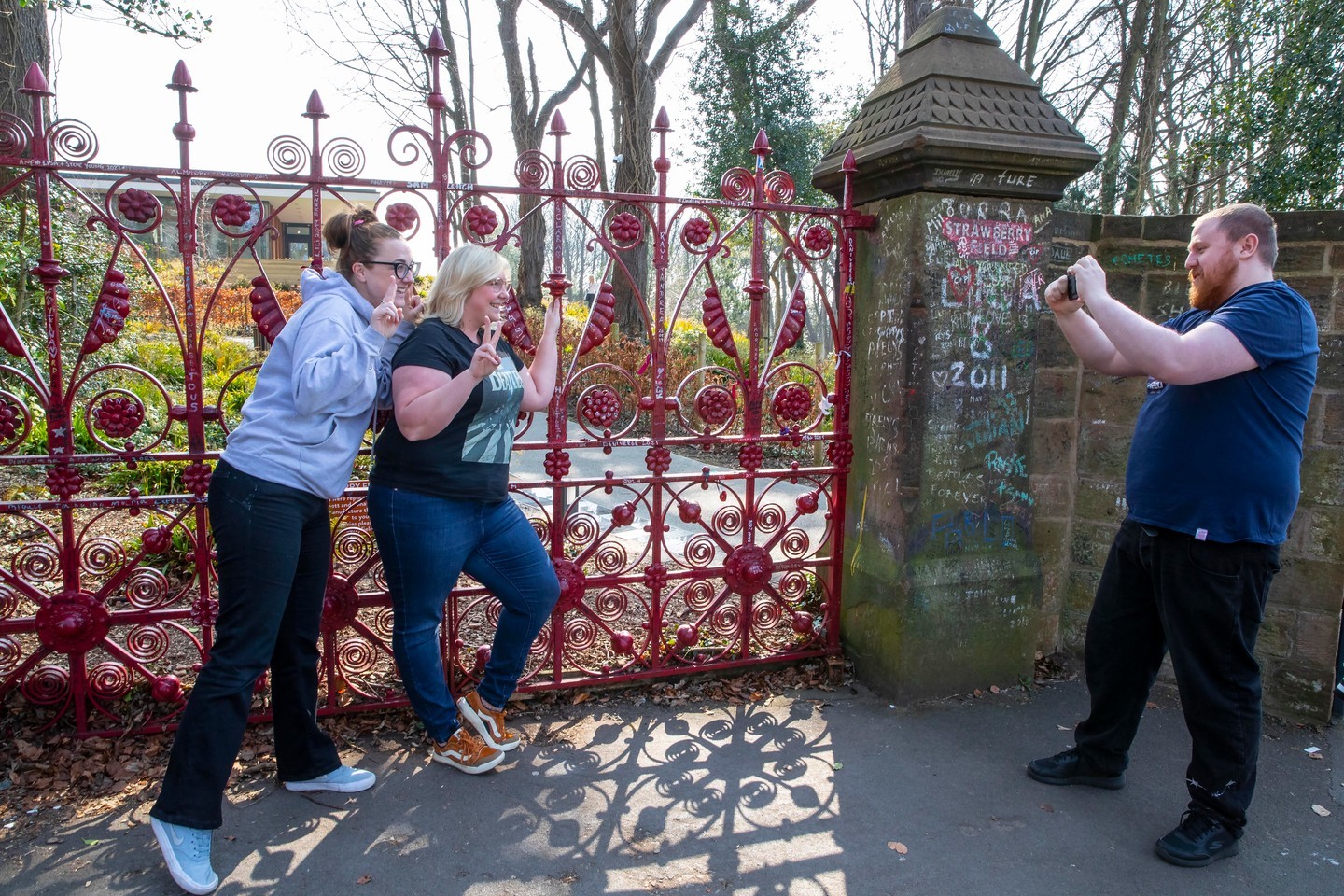 Two women pose in front of the red gates at the Strawberry Field garden.