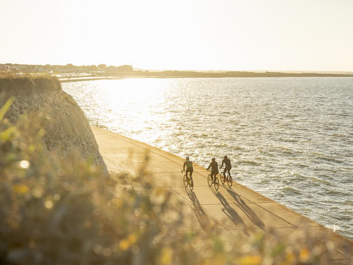 Three cyclists on a coastal path during sunset