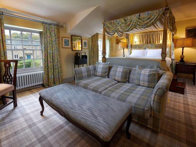 Bedroom at the Devonshire Arms at Pilsley, Derbyshire with a grey tartan upholstered sofa and large foot stool in the foreground, matching tartan carpet and floral curtains and matching draped four-poster bed in the background.