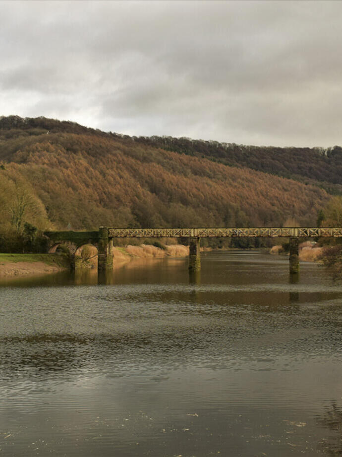 Eine Brücke aus Stein und rostigem Metall über einen breiten Fluss auf dem Land im Herbst.