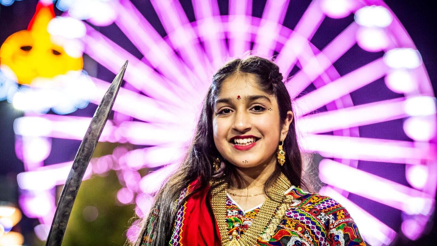 A woman celebrating Divali in front of a large lit up wheel