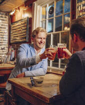 Two men sat in a pub toasting each other with pints of beer