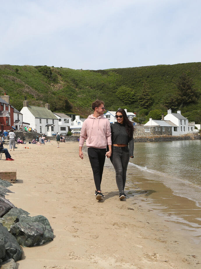 Deux personnes marchant le long d'une plage de sable avec l'océan d'un côté et des pubs et des magasins de l'autre.