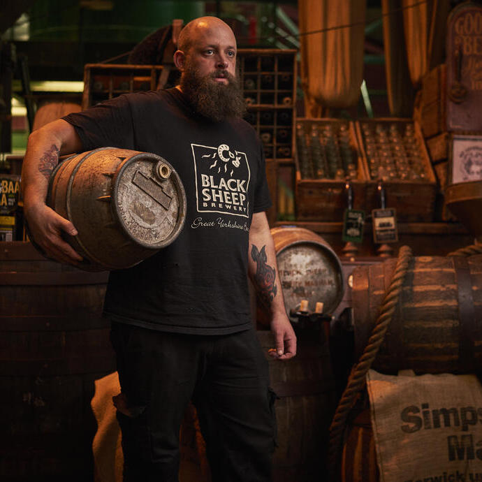 Hombre de pie en un almacén, sosteniendo un barril de cerveza de madera