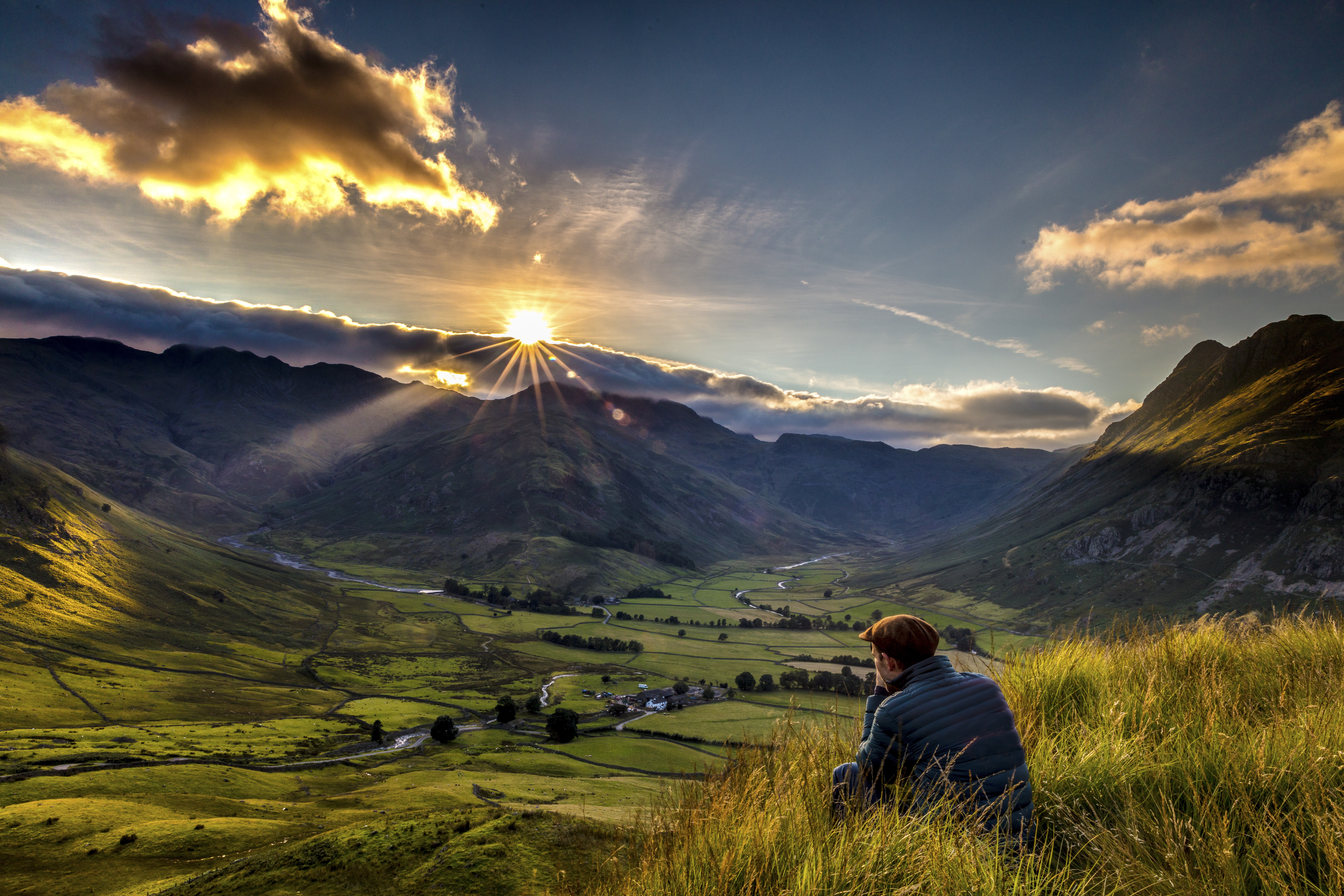 Hombre sentado en la hierba alta al borde de una colina contemplando la puesta de sol.