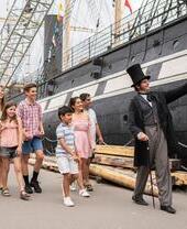 Guide dressed up in 19th century costume showing historic ship to a group of visitors