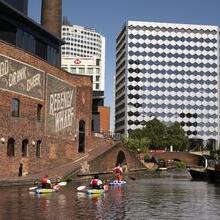 Group of people paddleboarding past industrial buildings on a canal