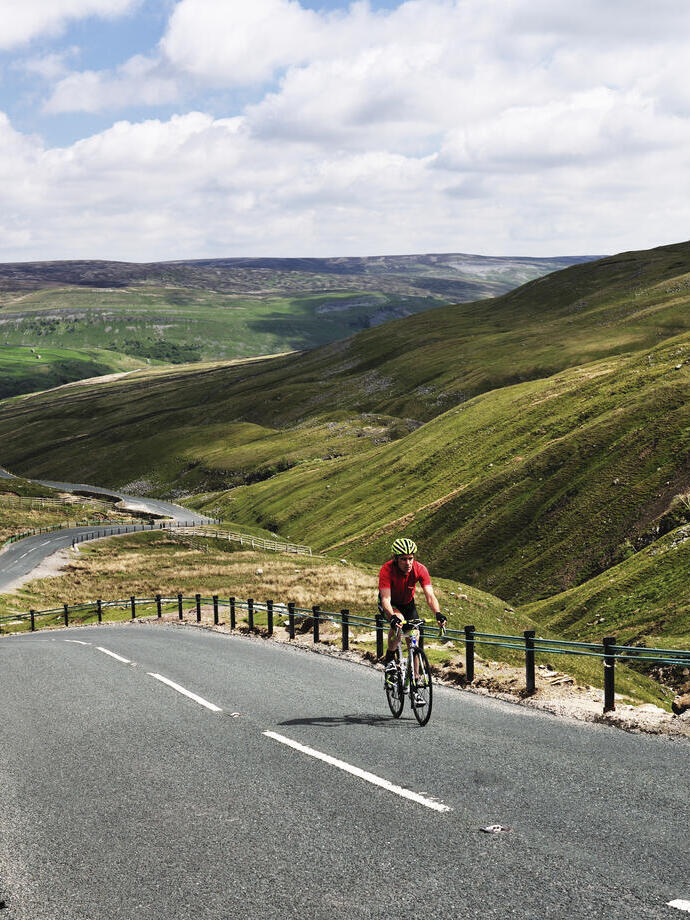 Cyclist riding on road through green dales