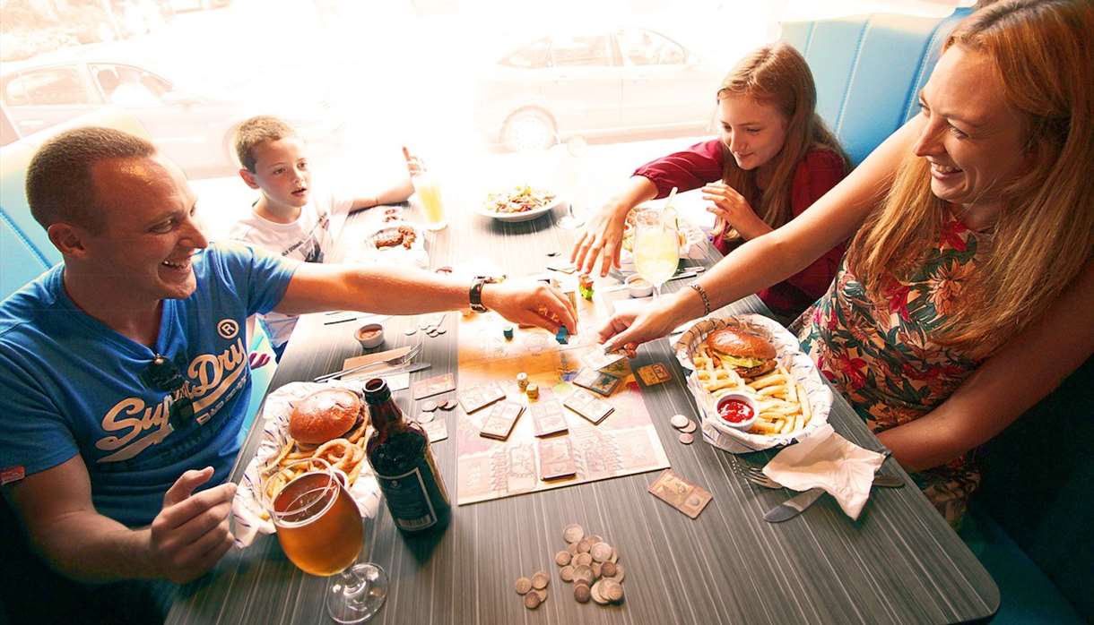 A family playing a board game while eating food at a cafe while playing board games