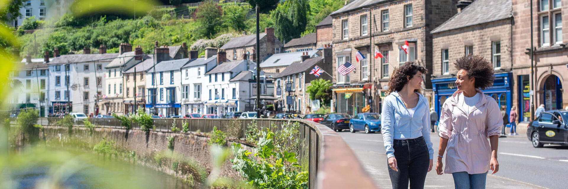 Two women walk down a main street in a hillside town