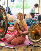 A woman on a yoga mat holding a pair of mallets and preparing to hit a set of gongs
