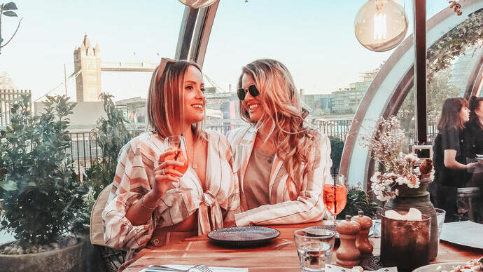Twee vrouwen genieten van eten en drinken in een glazen eetcabine aan de rivier