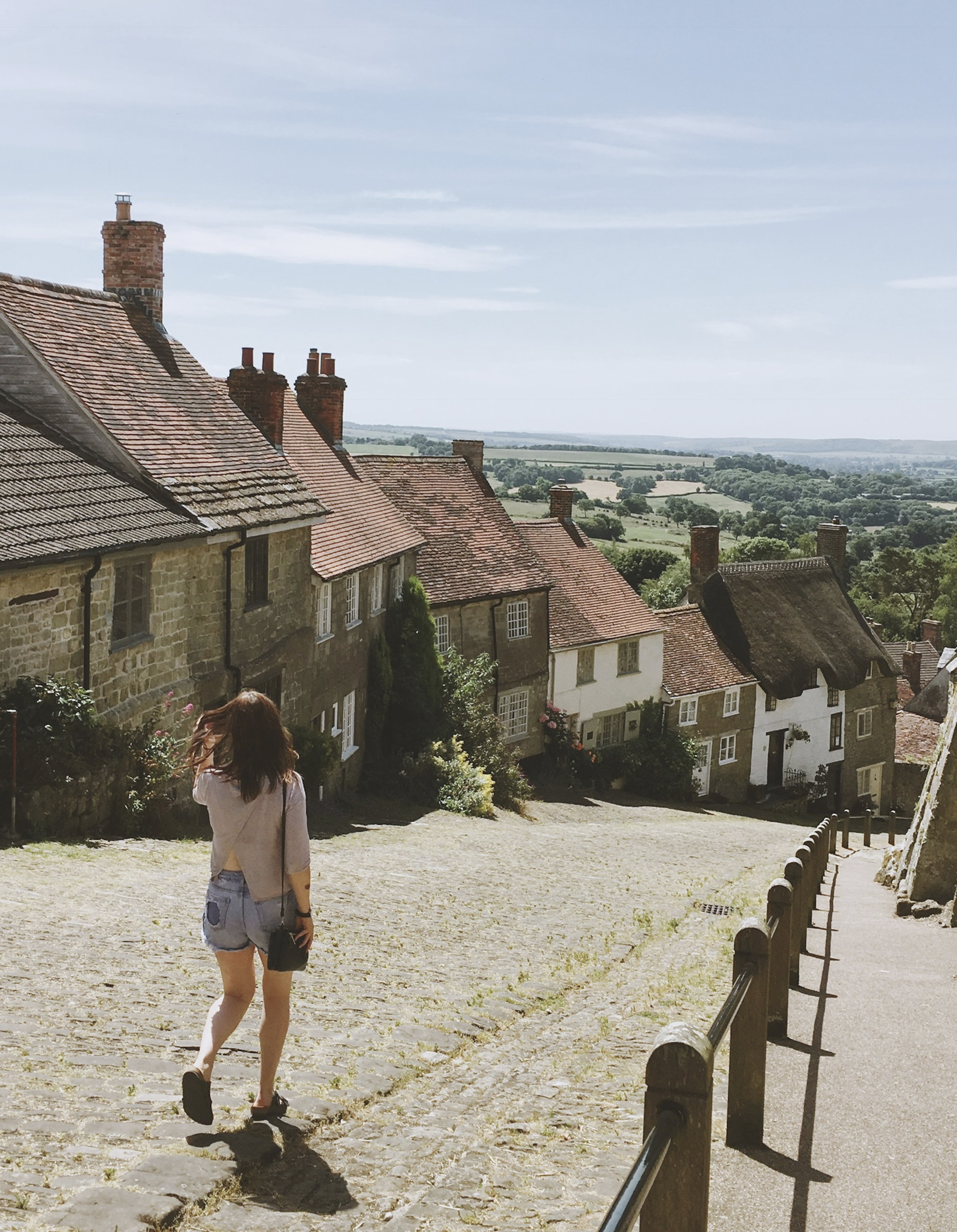 Mujer caminando por una empinada calle empedrada de un pueblo en verano