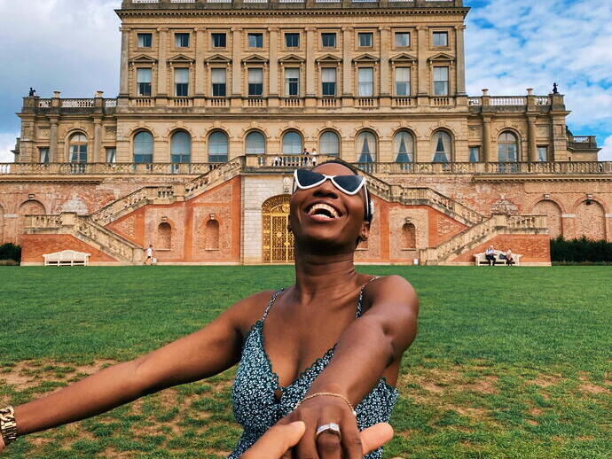 Woman laughing sitting on the grass in front of a stately home