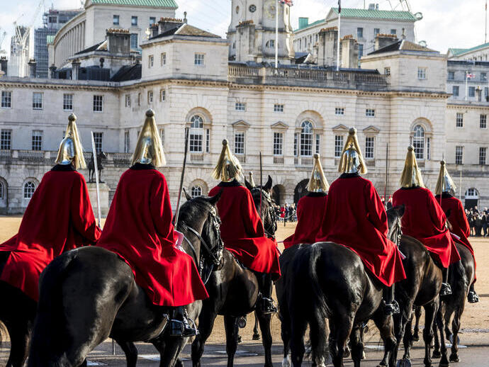 Hommes en uniforme de cérémonie chevauchant des chevaux en direction d'un grand bâtiment historique et d'une grande roue