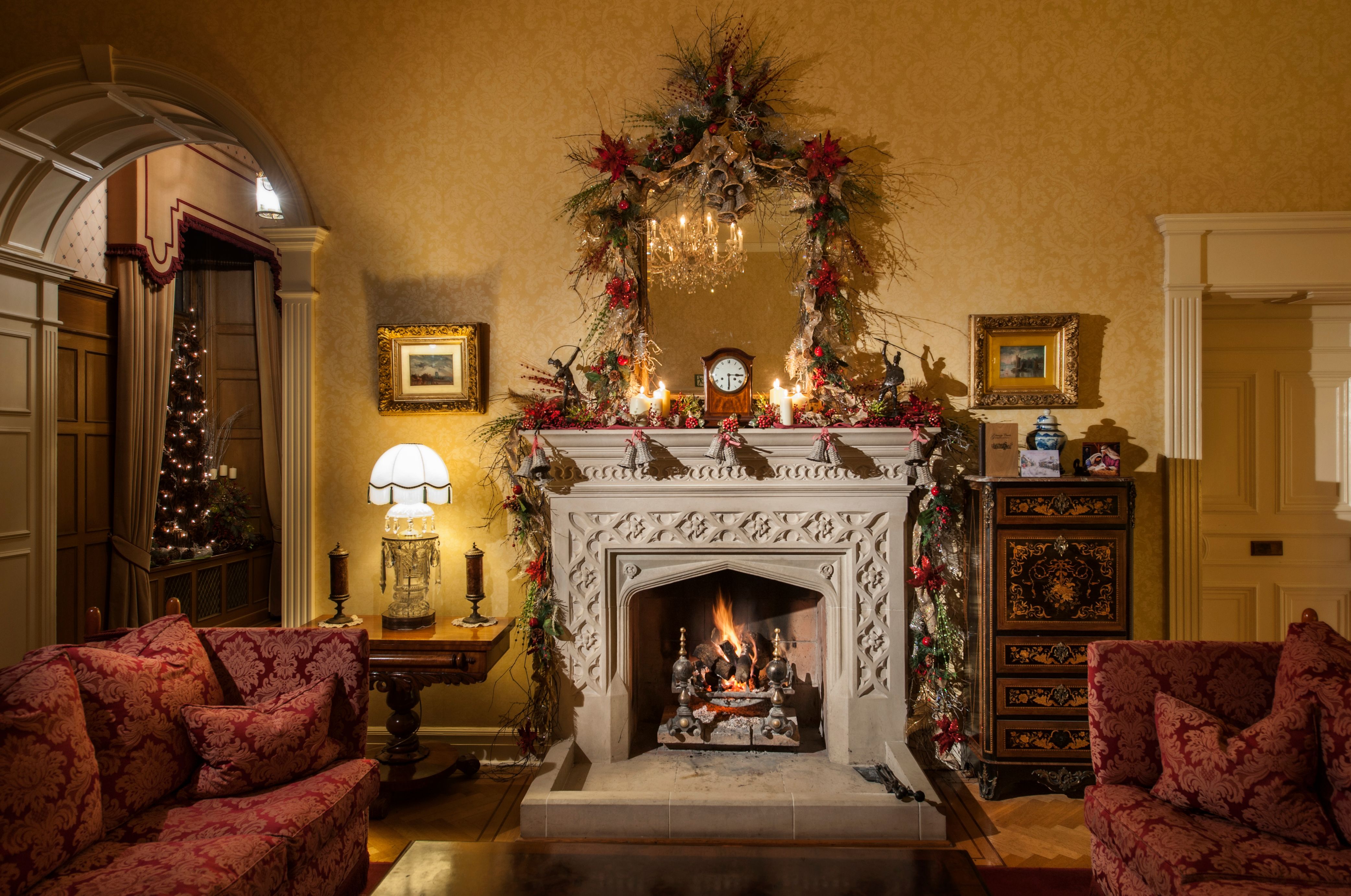 Traditionelles Wohnzimmer mit Weihnachtsdekoration, brennendem Kamin und zwei roten Sofas.