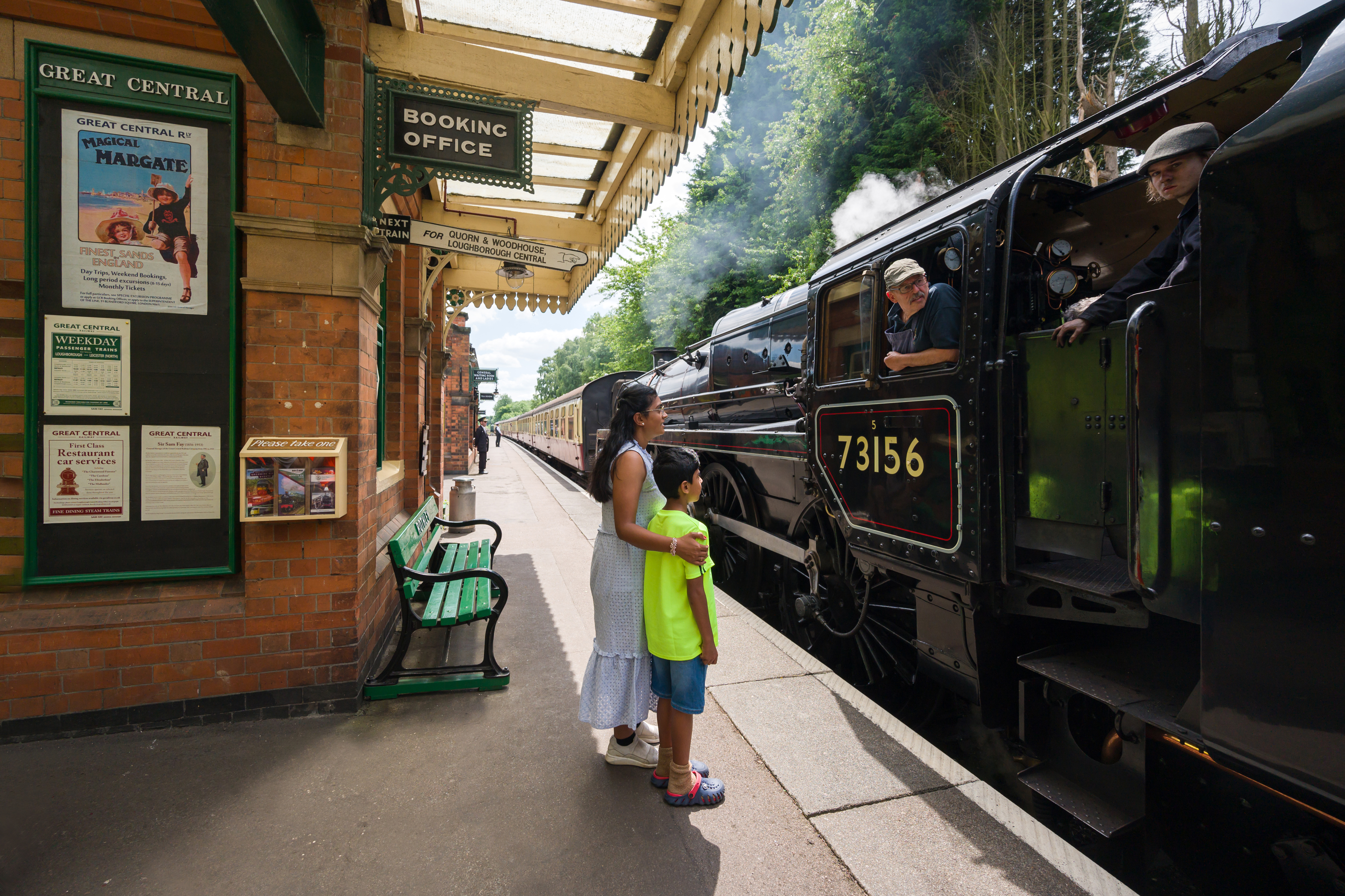A woman and her son stand on a railway platform by a steam train
