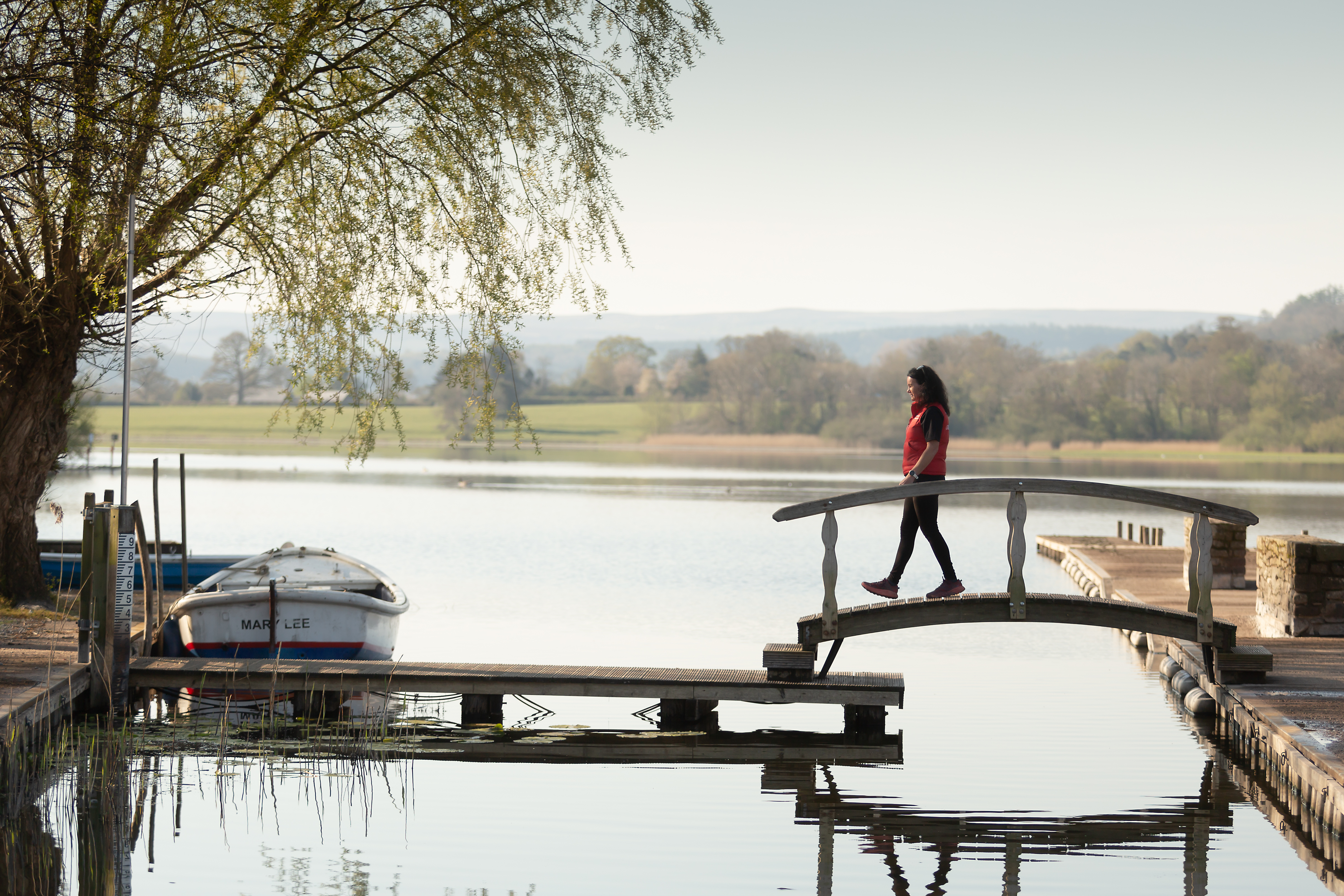 A woman stepping over a bridge, near a moored boat.