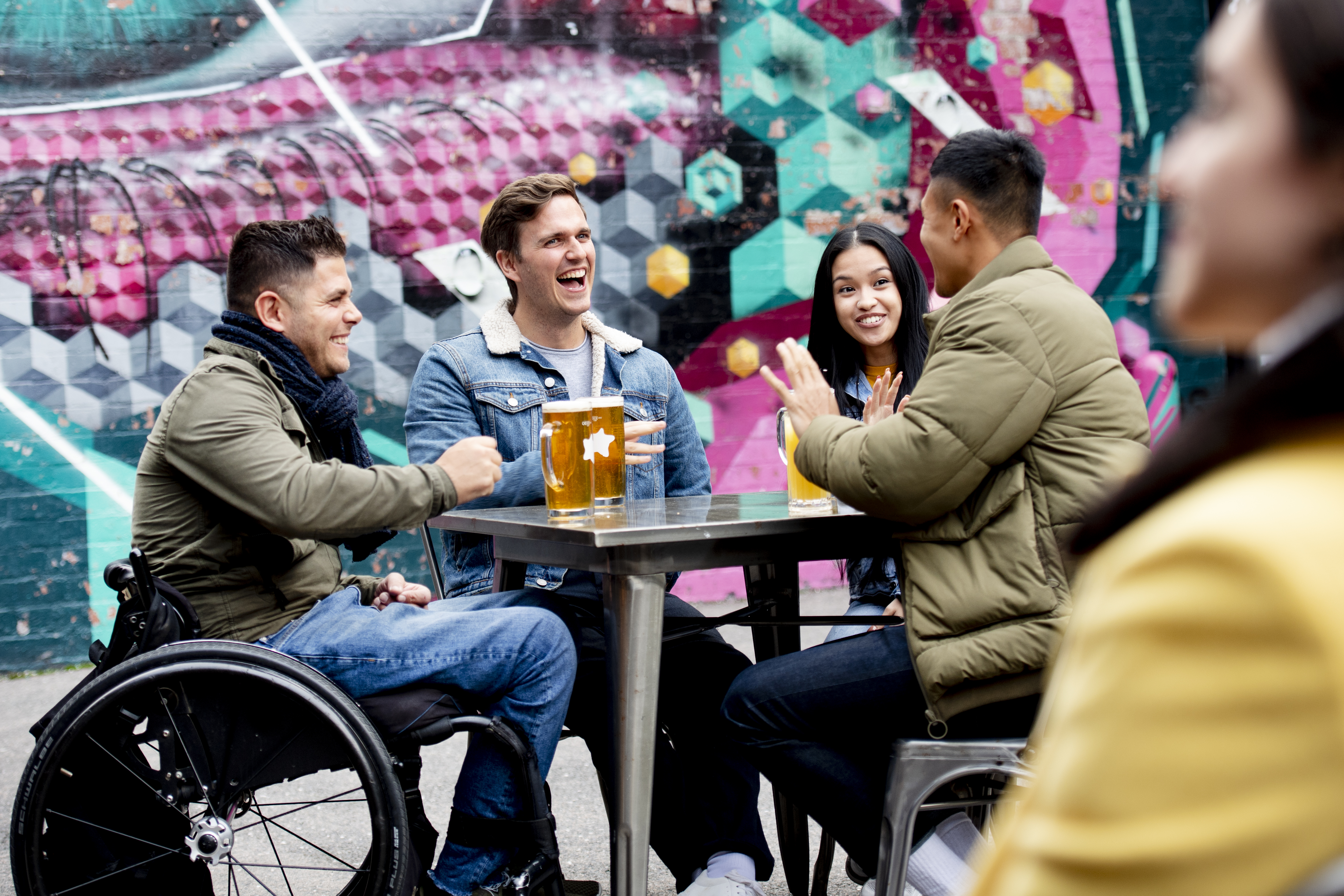 Amigos, entre ellos un hombre en silla de ruedas, tomando una cerveza en una terraza al aire libre